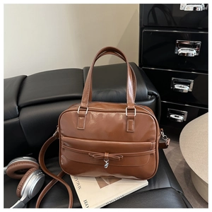 Close-up of caramel leather handbag featuring a bow detail and silver metal pendant