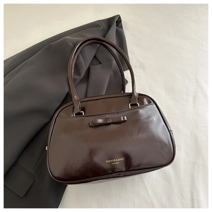 Detail of dark brown glossy pillow bag with bow decoration and gold logo text