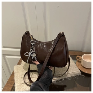 Detail of dark brown arched shoulder bag with metallic bow charm and crinkled texture