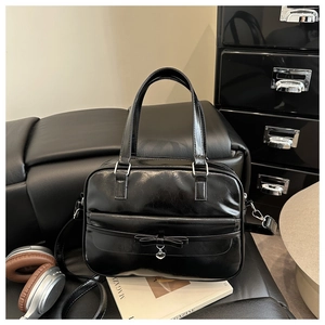 Detail of black glossy faux leather tote bag with bow accent and heart pendant charm