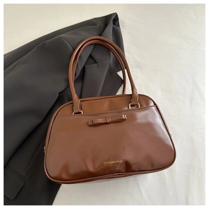 Close-up of caramel brown glossy shoulder bag with a stylish bow and gold lettering