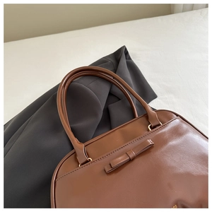 Detail of a brown glossy leather shoulder bag featuring a sweet bow and gold hardware