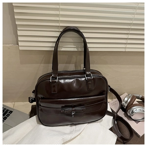 Detail of dark brown glossy patent leather bag with bow accent and silver metal charm