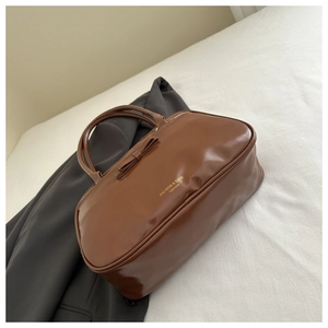 Close-up of brown glossy faux leather shoulder bag with decorative 3D bow and gold lettering