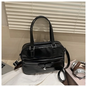 Detail of a black glossy tote bag featuring a bow charm and adjustable shoulder strap