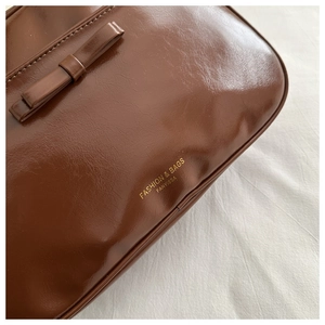 Detail of dark brown leather handbag with a bow decoration and gold embossed lettering