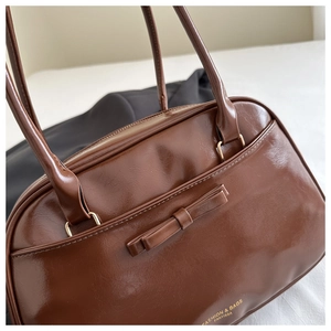 Detailed view of brown retro underarm bag with glossy leather finish and bow decoration