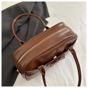 Detail of dark brown glossy leather handbag featuring top zipper and leather bow decoration
