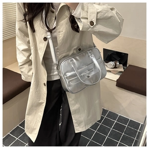 Detailed top view of a metallic silver rectangular handbag held by a model in a trench coat