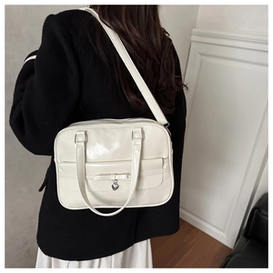 Detail of creamy white glossy shoulder bag with bow and silver heart pendant charm