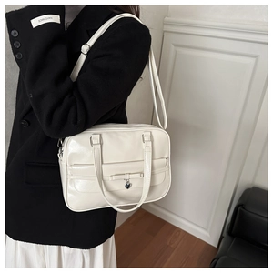 Detail of off-white glossy leather bag featuring bow tie and silver heart pendant charm