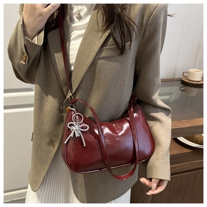 Detail van de wijnrode baguette-tas met zilveren strikhanger en glanzende afwerking