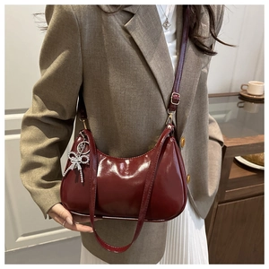 Detail of burgundy glossy leather hobo bag with a silver rhinestone bow charm accessory