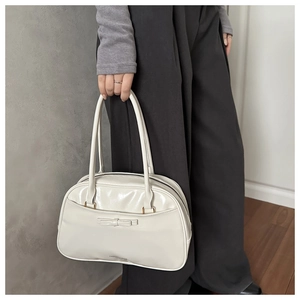 Detail of white glossy tote bag with bow decoration held by model in minimalist indoor setting