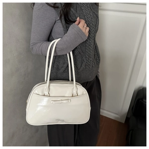 Close-up of cream glossy shoulder bag featuring a stylish bow and elegant slim handles