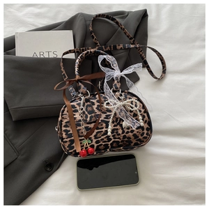 Detail of leopard print handbag featuring cherry and pearl bow charms on a dark blazer