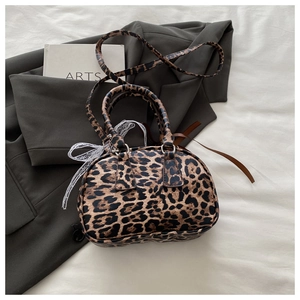 Detail of leopard print boston bag featuring a white lace bow and adjustable strap