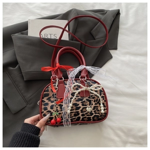 Detail of leopard print handbag featuring red leather handles and cherry pendant decorations