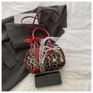 Detail view of leopard print handbag with red straps, lace, and cherry pendant