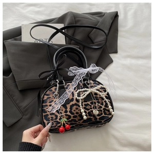 Detail of leopard print handbag with cherry and pearl charms on grey blazer backdrop