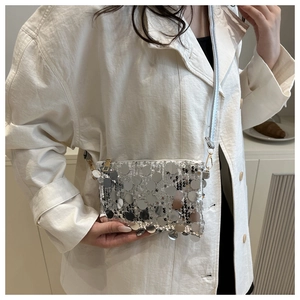 Detailed view of a silver sequin crossbody bag with a metallic finish on a model coat