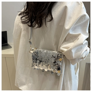 Close-up of silver sequin crossbody bag with chain strap worn by a model in office setting