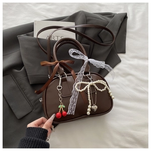 Detail of dark brown handbag with lace bows, cherry charms, and pearl accessories