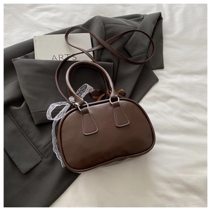 Detail of a dark brown bowling bag with white lace ribbon on a dark grey blazer