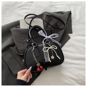 Detail of black cylindrical crossbody bag with red cherry charm and lace bow decor
