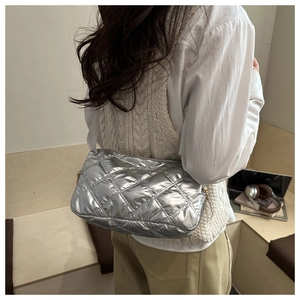 Detailed back view of a silver quilted puffer crossbody bag worn by a model in a room