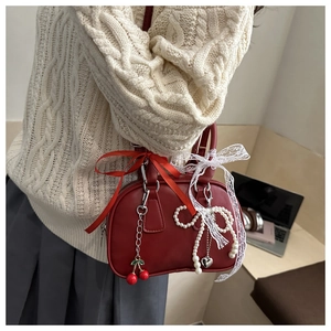 Detail of red leather Boston handbag with pearl bow and cherry charms on a model