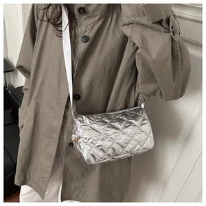 Detail of silver quilted crossbody bag with rhombic stitching on a model in beige trench coat