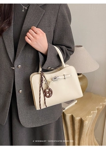 Detail of off-white lychee grain handbag with metal turn-lock and pretzel charm accessory