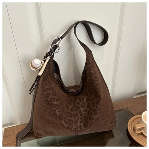 Close-up of leopard print tote bag with suede texture and baseball bat charm on a table