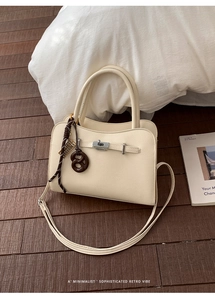 Detail of beige textured leather handbag with silver lock and pretzel pendant on wood floor
