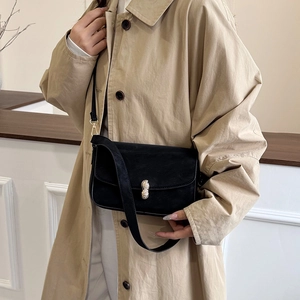 Minimalist black shoulder bag with gold peanut-shaped buckle on beige trench coat