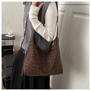 Detail of a large leopard print hobo bag with a dark brown leather strap worn by a model