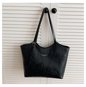 Detail of black pleated leather tote bag with gold lettering hanging on a white door