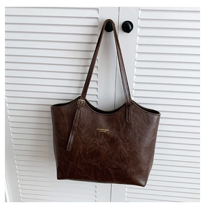 Detail of dark brown tote bag with gold lettering hanging on white closet door handle