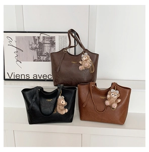Three textured tote bags in brown and black with bear charms on display