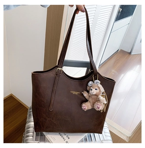 Detailed close-up of dark brown leather tote bag with gold text and plush bear charm