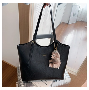 Detail of black tote bag with lychee texture and purple plush bunny charm on silver suitcase