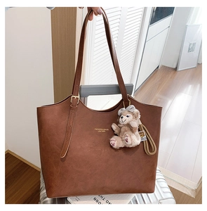 Detail of caramel leather tote bag with bear charm hanging on a luggage suitcase handle