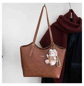 Detailed view of brown leather tote bag with vintage texture and plush bear charm accent