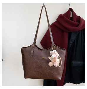 Detail of dark brown leather tote with gold logo text and fuzzy bear keychain accessory