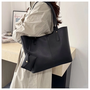 Macro detail of large black tote bag with small matching pouch on cream shirt background