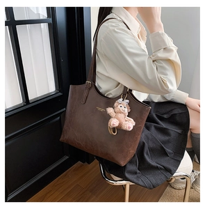 Close-up of a large dark brown leather tote bag with gold lettering and a plush bear charm