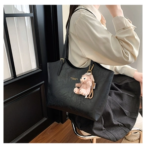 Detailed view of black pebbled leather tote with gold text and pink plush bear charm