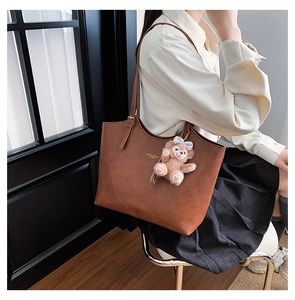 Close-up of a vintage brown leather tote bag with a pink plush bear charm accessory