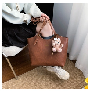 Close-up of brown leather tote bag featuring elegant lettering and a plush bear charm